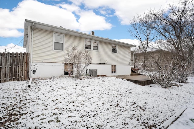 snow covered back of property with cooling unit, a chimney, and fence