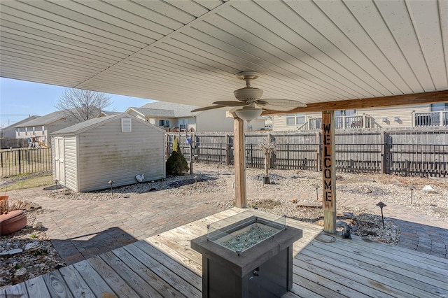 wooden deck featuring ceiling fan, an outbuilding, a fenced backyard, a fire pit, and a storage unit