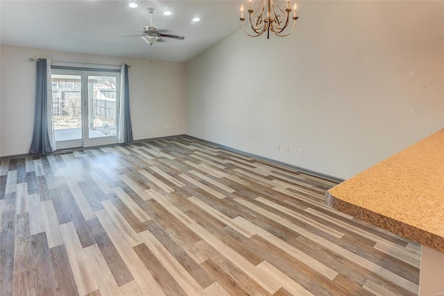 empty room with light wood finished floors, recessed lighting, baseboards, and ceiling fan with notable chandelier