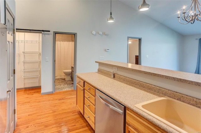 kitchen with decorative light fixtures, light wood finished floors, light countertops, stainless steel dishwasher, and a sink