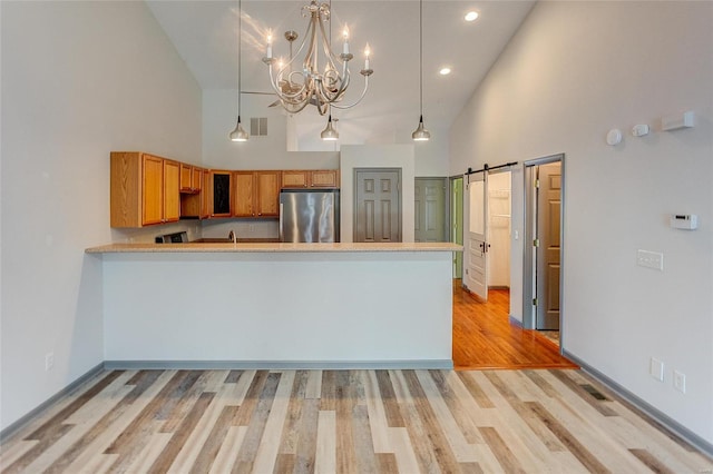 kitchen with light wood finished floors, a towering ceiling, a barn door, freestanding refrigerator, and a peninsula