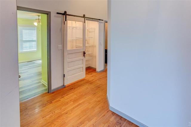 corridor with light wood-style flooring, baseboards, and a barn door