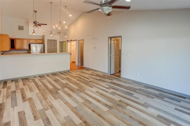 unfurnished living room featuring light wood finished floors, a barn door, visible vents, a ceiling fan, and high vaulted ceiling