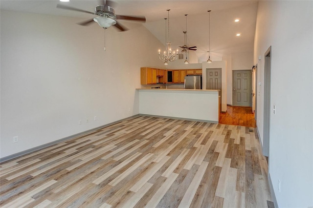 unfurnished living room with ceiling fan with notable chandelier, high vaulted ceiling, and light wood finished floors