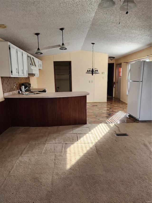 kitchen with light carpet, a peninsula, visible vents, freestanding refrigerator, and pendant lighting