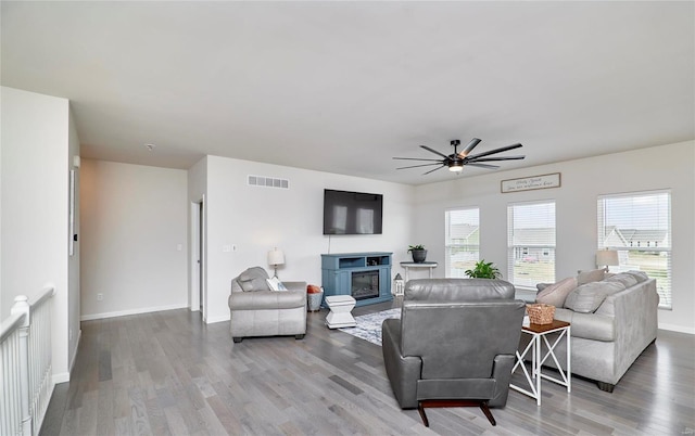 living room featuring visible vents, baseboards, wood finished floors, a glass covered fireplace, and a ceiling fan