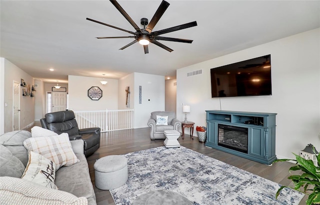 living room featuring dark wood-style floors, baseboards, visible vents, ceiling fan, and a glass covered fireplace