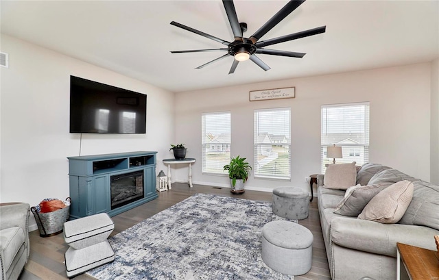 living area featuring visible vents, baseboards, a glass covered fireplace, a ceiling fan, and dark wood-style flooring