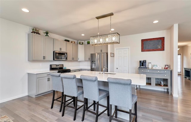 kitchen with appliances with stainless steel finishes, a breakfast bar area, light countertops, and gray cabinetry