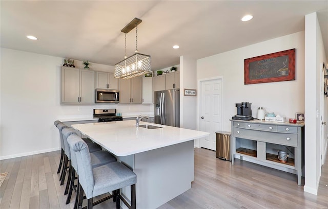 kitchen featuring gray cabinetry, a breakfast bar area, light countertops, appliances with stainless steel finishes, and a sink