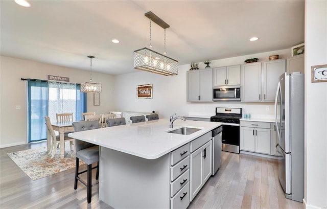 kitchen featuring a sink, light wood-type flooring, appliances with stainless steel finishes, a kitchen breakfast bar, and a kitchen island with sink