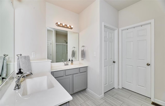 full bathroom featuring a stall shower, two vanities, baseboards, and a sink