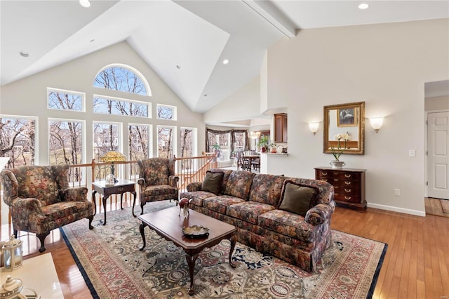 living room with beam ceiling, light wood-style flooring, high vaulted ceiling, and baseboards