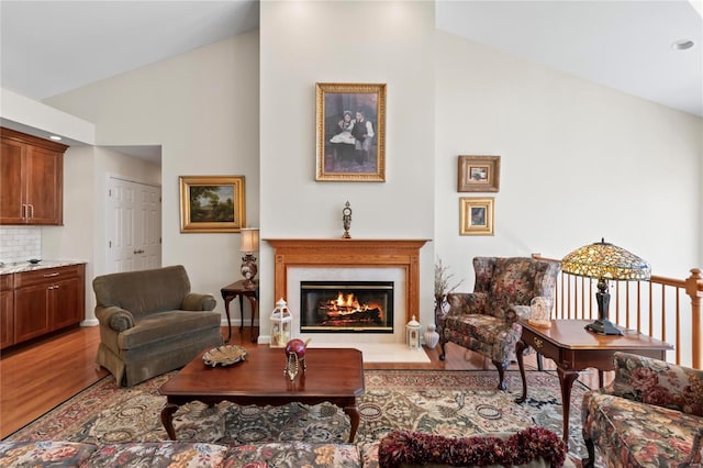 living area featuring a glass covered fireplace, baseboards, high vaulted ceiling, and light wood-style flooring