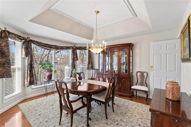 dining area with a tray ceiling, wood finished floors, baseboards, and a chandelier