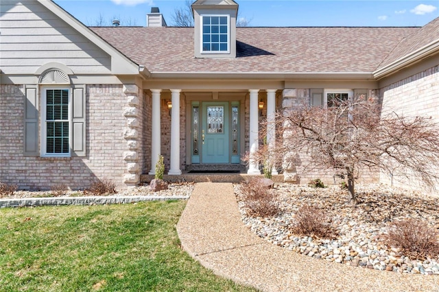 doorway to property featuring a lawn, brick siding, roof with shingles, and a chimney