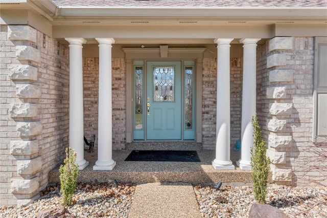 doorway to property with brick siding, a porch, and a shingled roof