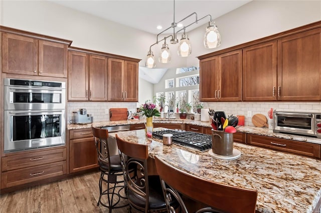 kitchen with a breakfast bar area, light wood finished floors, decorative backsplash, vaulted ceiling, and appliances with stainless steel finishes