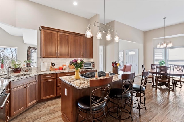 kitchen featuring stainless steel gas cooktop, an inviting chandelier, a sink, decorative backsplash, and light wood-type flooring