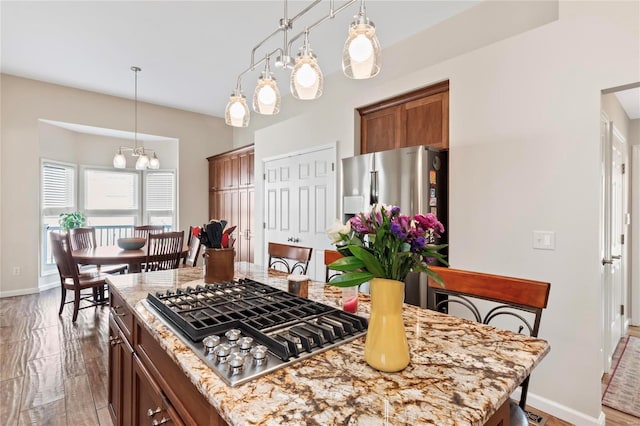 kitchen with light stone counters, brown cabinetry, a kitchen island, stainless steel appliances, and decorative light fixtures