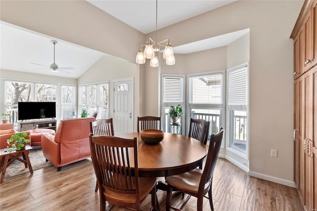 dining space featuring ceiling fan with notable chandelier, vaulted ceiling, light wood-style floors, and baseboards