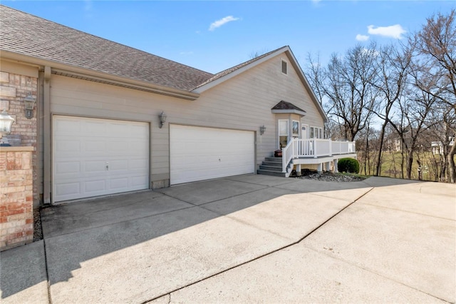 view of side of property with brick siding, driveway, a shingled roof, and a garage