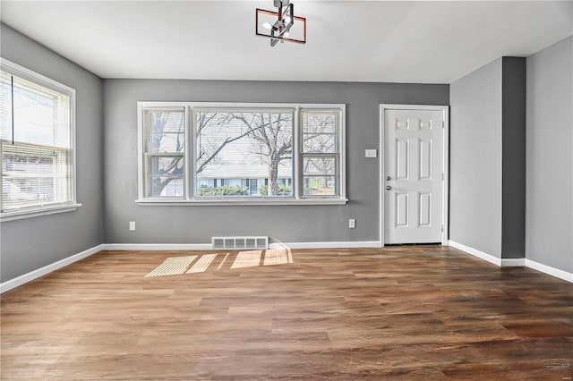 unfurnished room featuring wood finished floors, visible vents, and baseboards