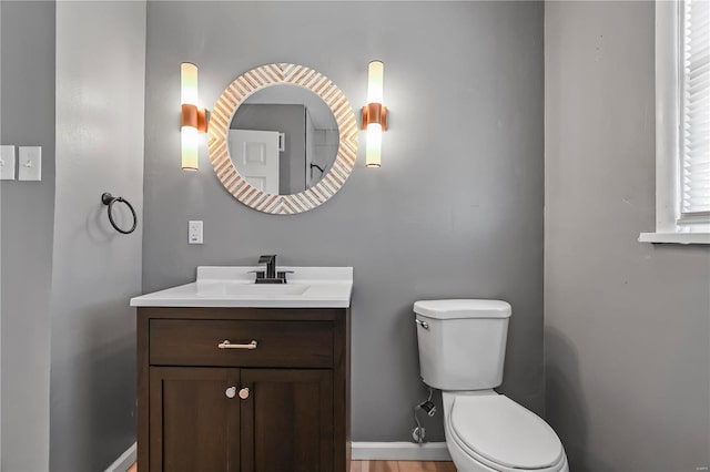 half bath with baseboards, toilet, and vanity