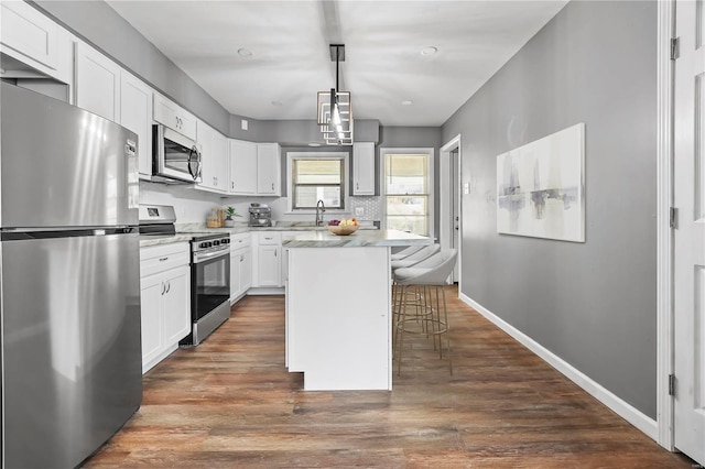 kitchen featuring dark wood-style flooring, light countertops, white cabinets, appliances with stainless steel finishes, and a kitchen breakfast bar