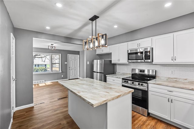 kitchen featuring a center island, dark wood finished floors, decorative backsplash, appliances with stainless steel finishes, and white cabinetry