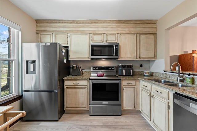 kitchen with a sink, appliances with stainless steel finishes, light wood finished floors, decorative backsplash, and light stone countertops