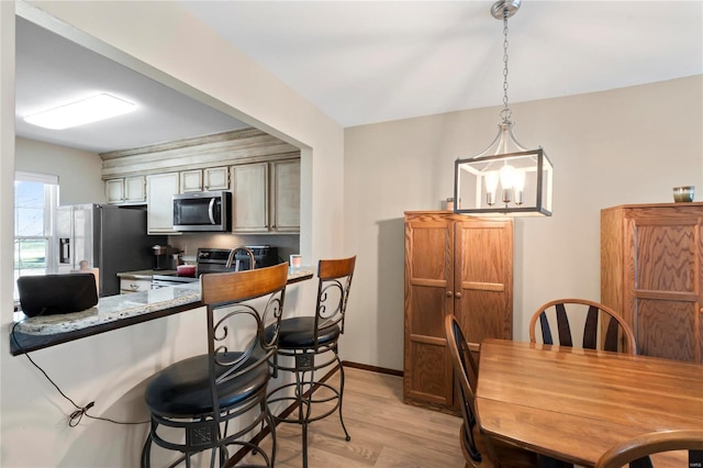 kitchen featuring a breakfast bar area, baseboards, light wood-style flooring, stainless steel appliances, and hanging light fixtures