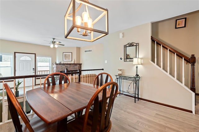 dining space with visible vents, a brick fireplace, baseboards, stairs, and light wood-type flooring