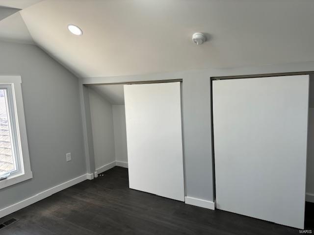 unfurnished bedroom with dark wood-type flooring, visible vents, baseboards, vaulted ceiling, and two closets