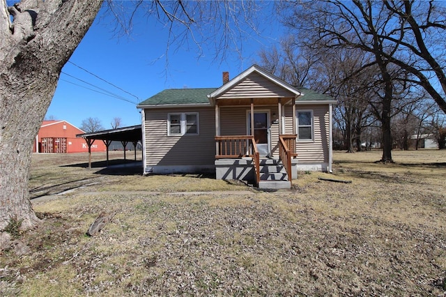 bungalow-style house with covered porch, a shingled roof, a chimney, and an attached carport