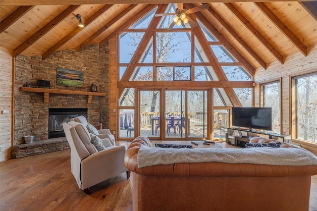 living area with a stone fireplace, beamed ceiling, wooden ceiling, and wood-type flooring