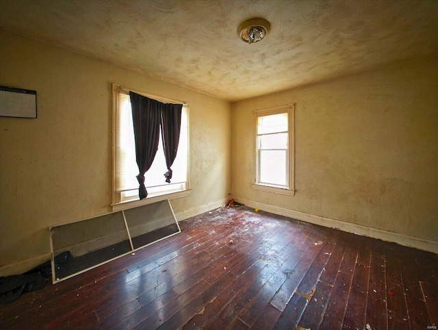 spare room featuring a textured ceiling, wood-type flooring, and baseboards