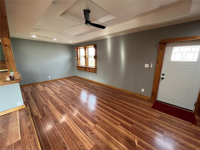 unfurnished living room with baseboards, ceiling fan, wood finished floors, a tray ceiling, and recessed lighting