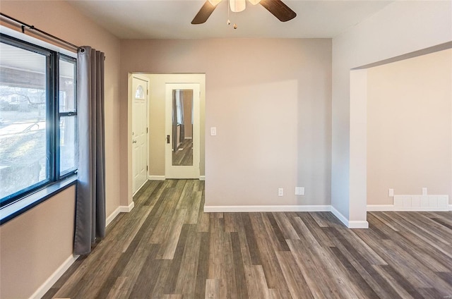 unfurnished room with dark wood finished floors, visible vents, a ceiling fan, and baseboards