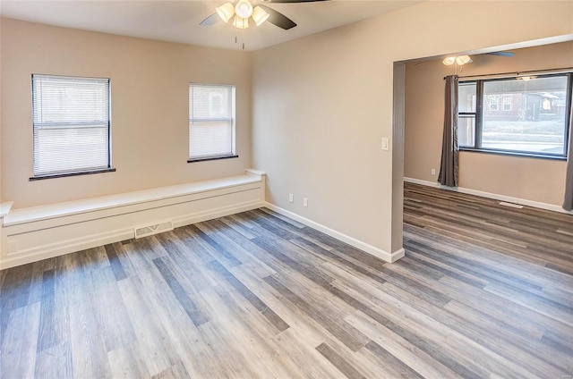 empty room featuring wood finished floors, a healthy amount of sunlight, visible vents, and baseboards