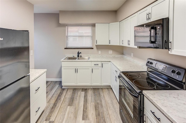 kitchen with a sink, light wood-style floors, black appliances, and white cabinetry