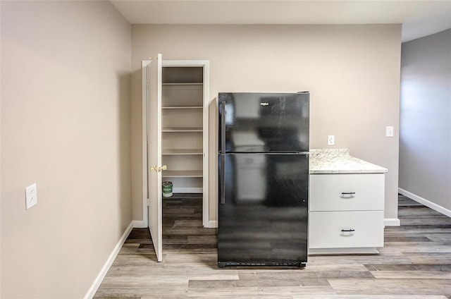 kitchen with light stone counters, baseboards, light wood-type flooring, and freestanding refrigerator