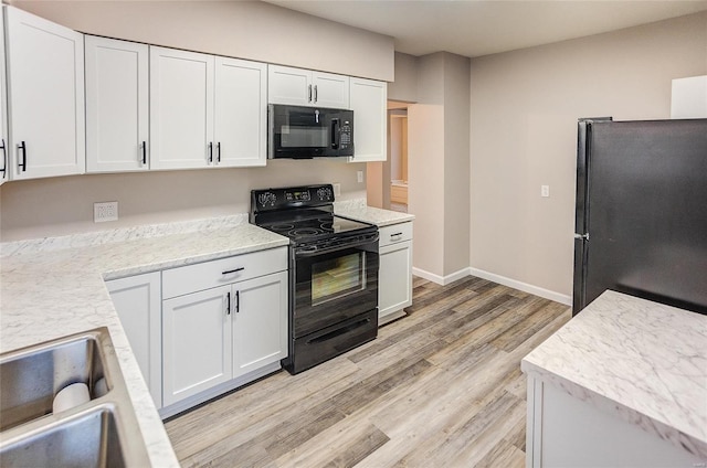 kitchen featuring light wood-style flooring, white cabinetry, black appliances, and baseboards