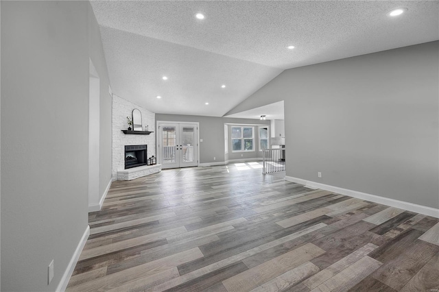 unfurnished living room featuring a fireplace, vaulted ceiling, wood finished floors, and french doors