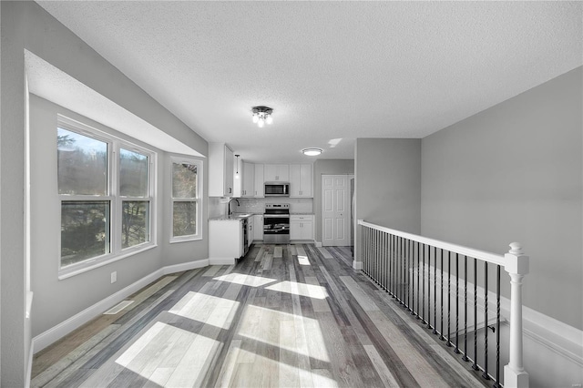 kitchen featuring light countertops, appliances with stainless steel finishes, white cabinetry, a sink, and wood finished floors