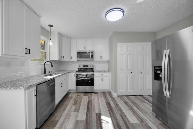 kitchen with appliances with stainless steel finishes, white cabinetry, a sink, and light wood-style flooring