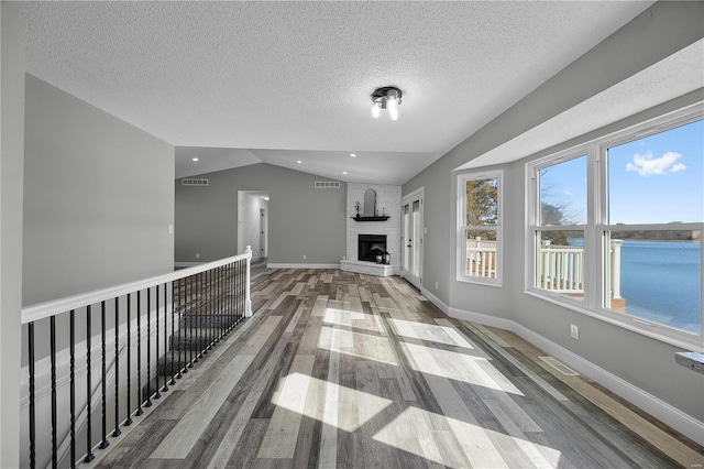 unfurnished living room with lofted ceiling, a fireplace, wood finished floors, visible vents, and baseboards