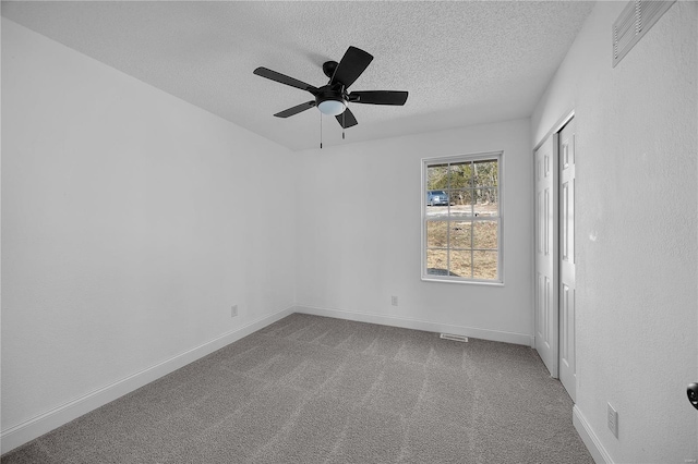 spare room featuring a textured ceiling, carpet floors, a ceiling fan, visible vents, and baseboards