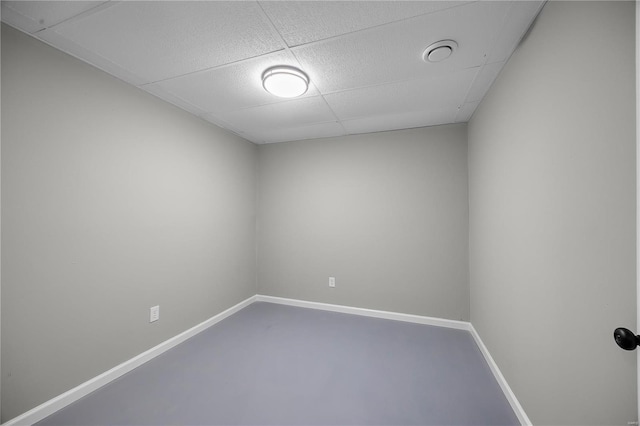 spare room featuring a drop ceiling, finished concrete flooring, and baseboards