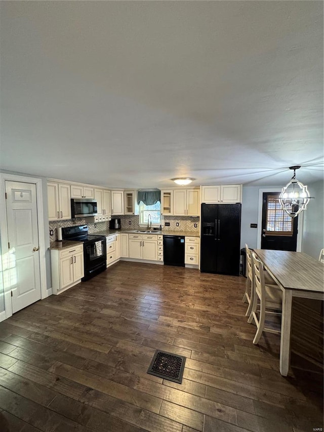 kitchen with dark wood-style flooring, decorative backsplash, cream cabinets, a sink, and black appliances